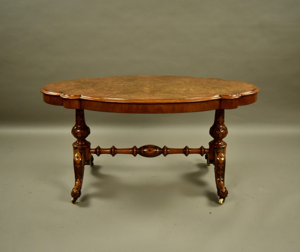 A Victorian burr walnut low coffee table featuring a shaped serpentine top, turned stretcher base, and inlaid legs on brass castors. View II
