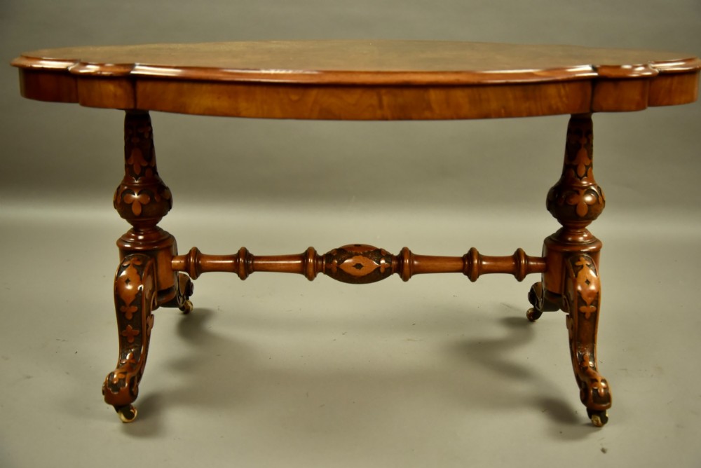 A Victorian burr walnut low coffee table featuring a shaped serpentine top, turned stretcher base, and inlaid legs on brass castors. View VI