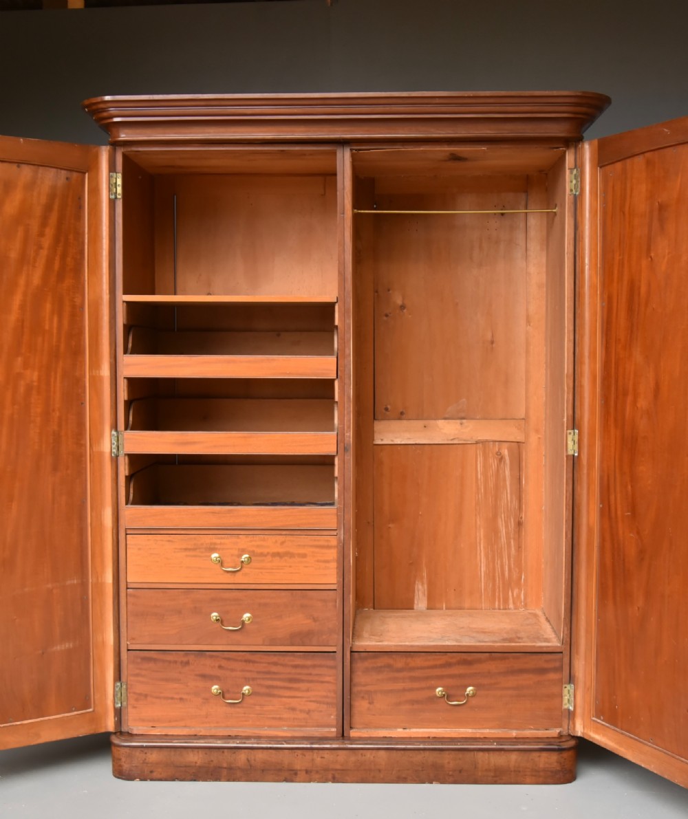 A Victorian flame mahogany double wardrobe featuring two arch-moulded panelled doors, a flared cornice, and a solid plinth base. View II