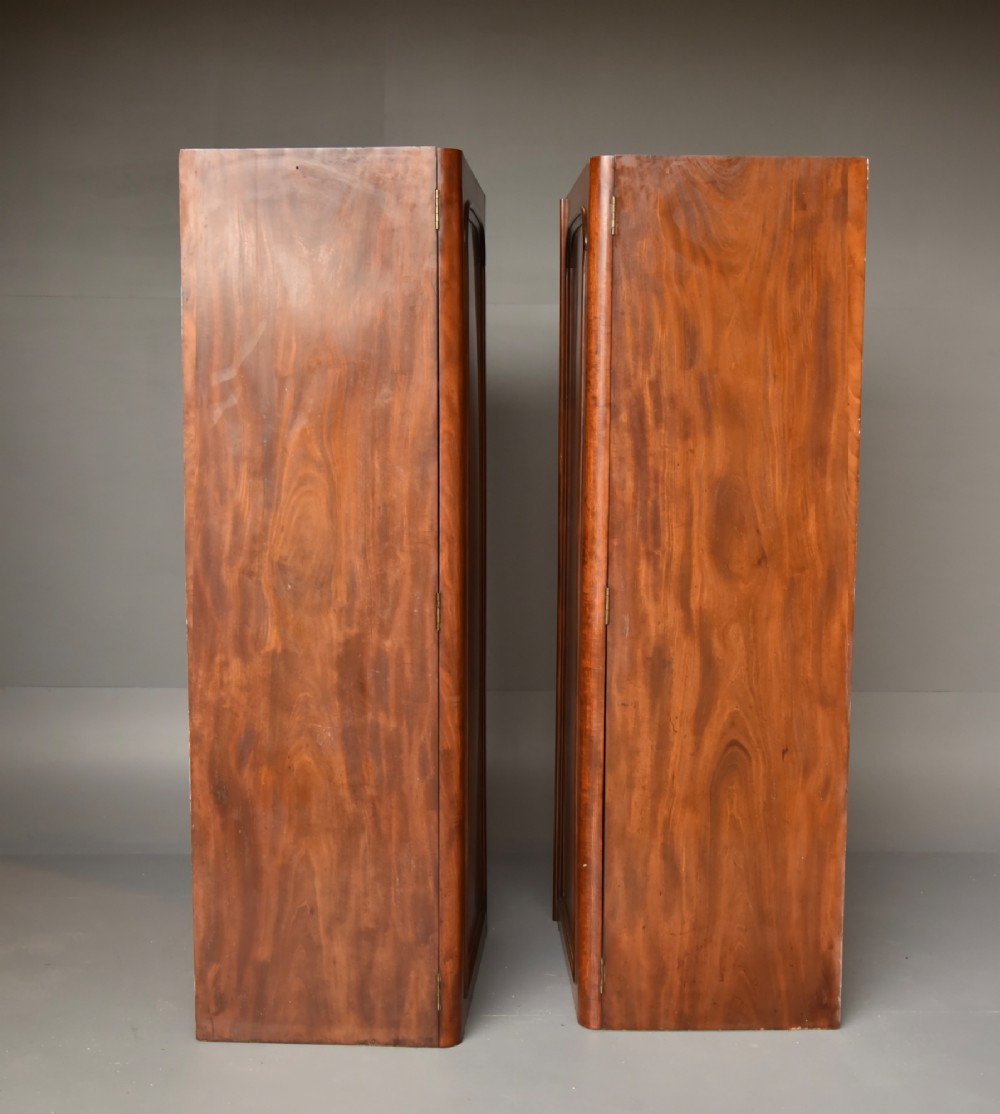 A Victorian flame mahogany double wardrobe featuring two arch-moulded panelled doors, a flared cornice, and a solid plinth base. View V