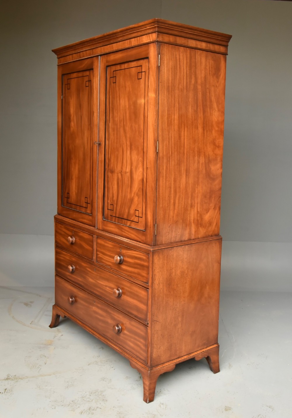 A Georgian mahogany gentlemans wardrobe featuring a two-door upper section with ebony line inlay over a base of two short and two long drawers on bracket feet. View II
