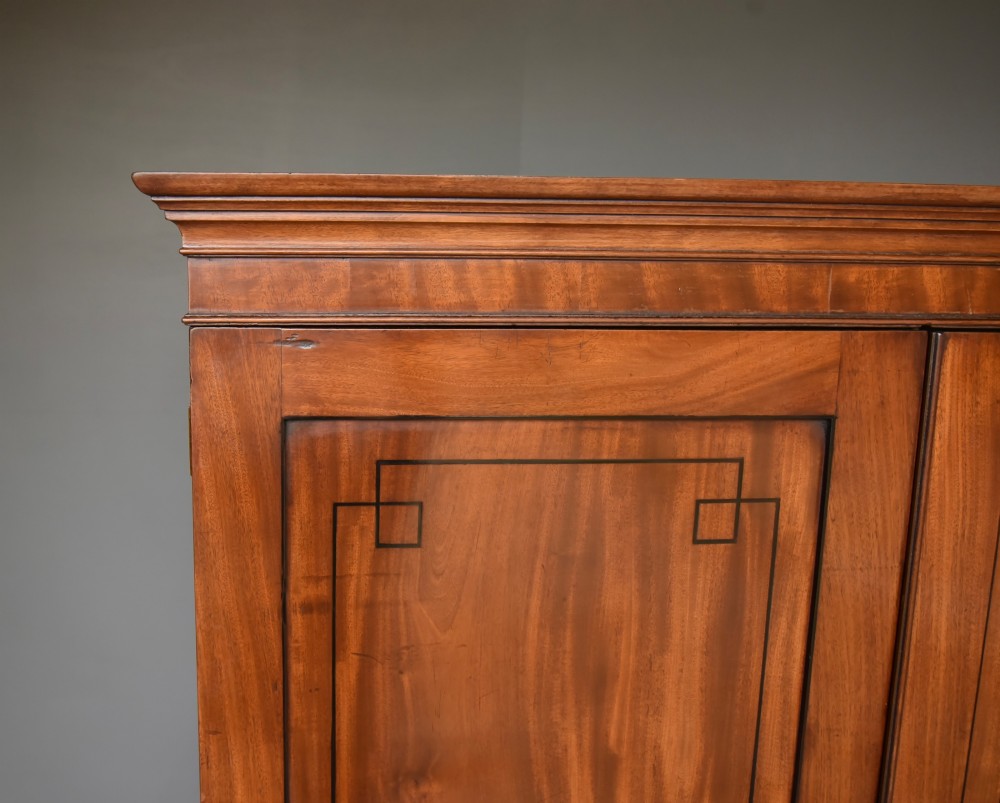 A Georgian mahogany gentlemans wardrobe featuring a two-door upper section with ebony line inlay over a base of two short and two long drawers on bracket feet. View V