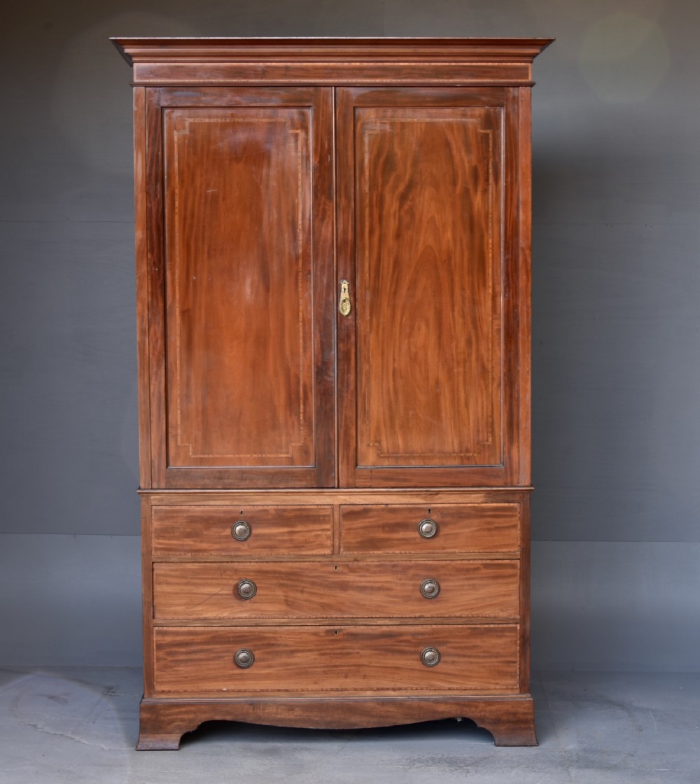 An Edwardian flame mahogany double wardrobe featuring two panelled cupboard doors with satinwood stringing set above two short and two long drawers with brass handles.
