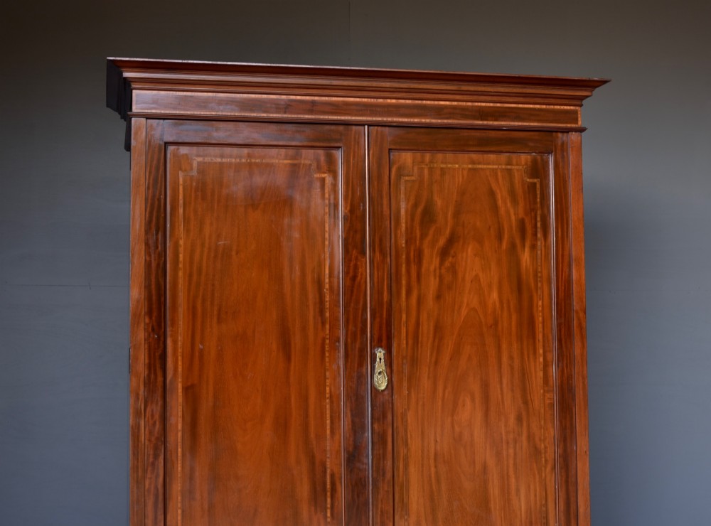An Edwardian flame mahogany double wardrobe featuring two panelled cupboard doors with satinwood stringing set above two short and two long drawers with brass handles. View III