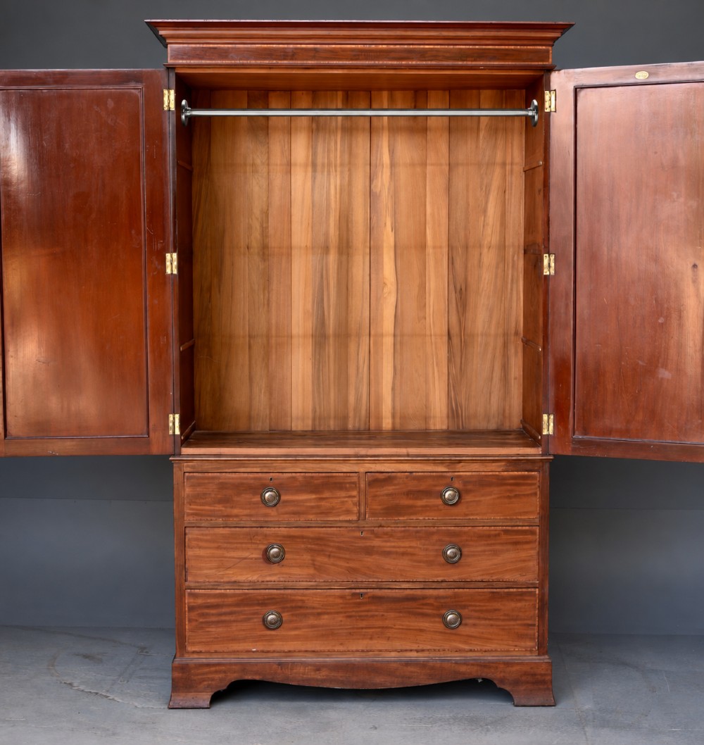 An Edwardian flame mahogany double wardrobe featuring two panelled cupboard doors with satinwood stringing set above two short and two long drawers with brass handles. View IV