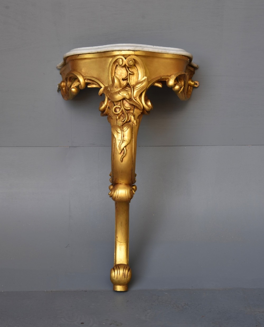 A 19th-century Rococo Revival wall-mounted giltwood console table with a single carved support leg featuring acanthus leaf scrolls and a shaped white marble top.
