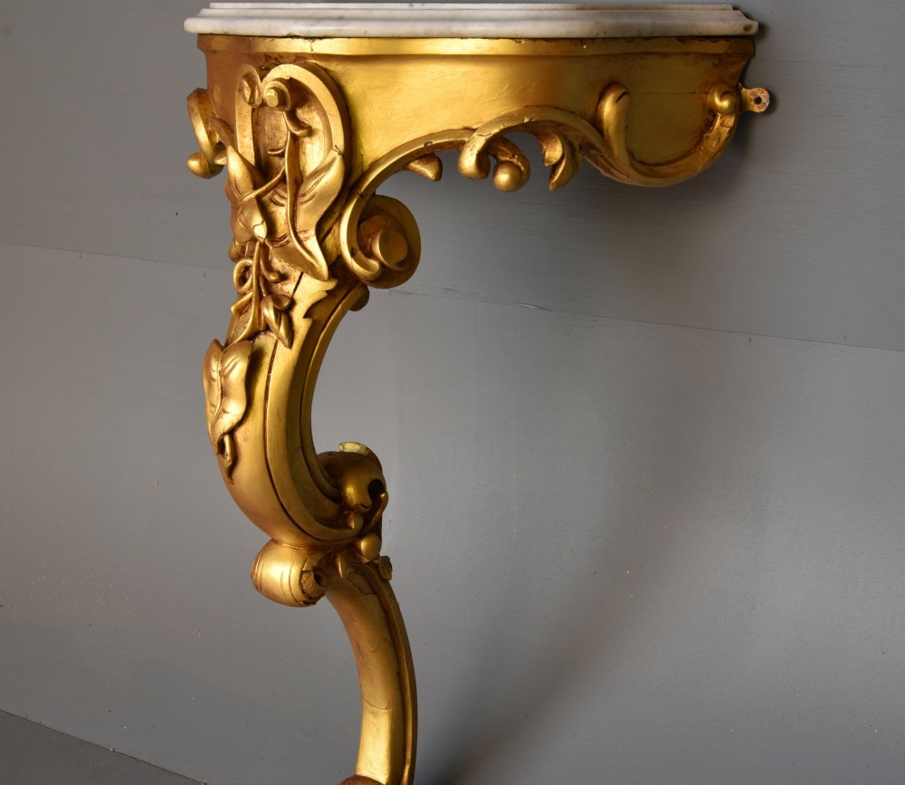 A 19th-century Rococo Revival wall-mounted giltwood console table with a single carved support leg featuring acanthus leaf scrolls and a shaped white marble top. View IV