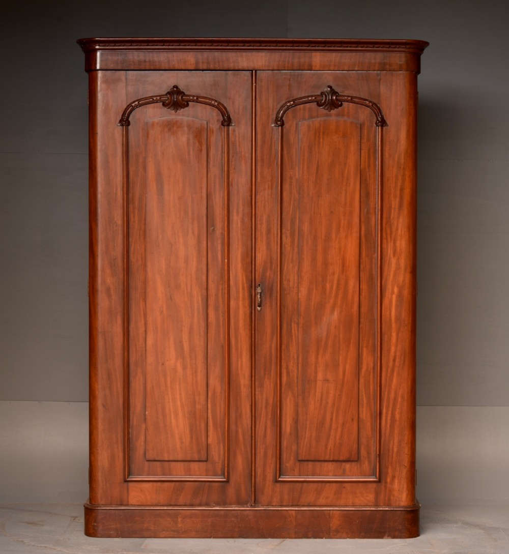 A tall Victorian mahogany double wardrobe with twin panelled doors topped by carved arch mouldings and supported on a plinth base.