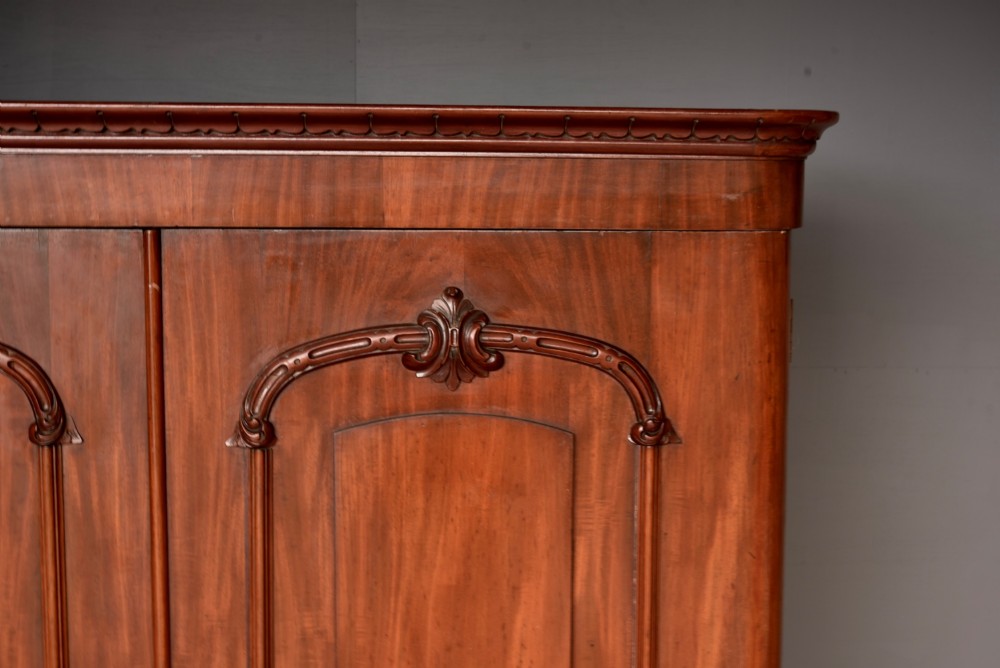 A tall Victorian mahogany double wardrobe with twin panelled doors topped by carved arch mouldings and supported on a plinth base. View III
