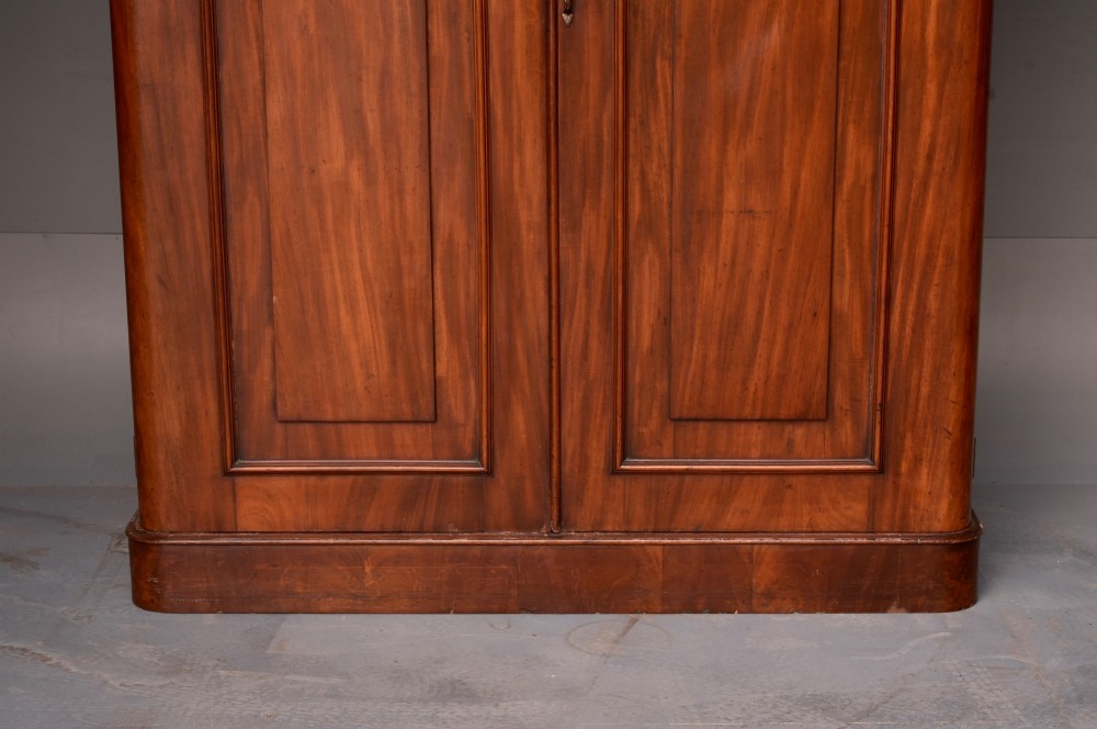 A tall Victorian mahogany double wardrobe with twin panelled doors topped by carved arch mouldings and supported on a plinth base. View IV
