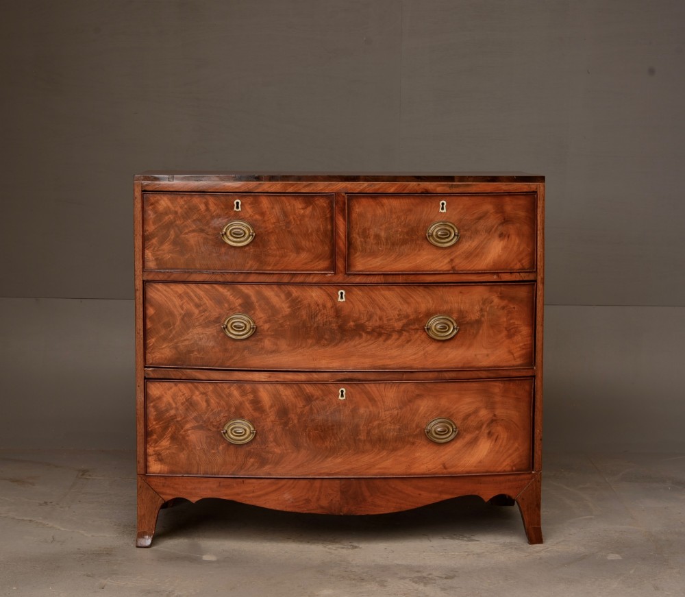 A Georgian flame mahogany bowfront chest of drawers featuring two short over two long drawers with brass ring handles and splayed bracket feet. View II