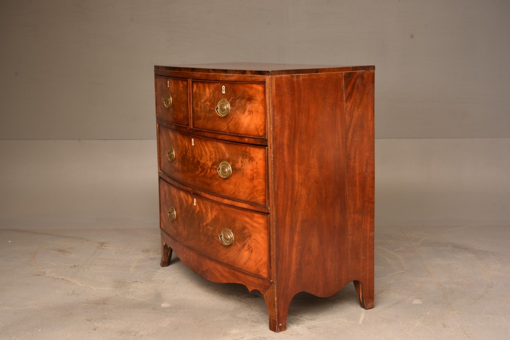A Georgian flame mahogany bowfront chest of drawers featuring two short over two long drawers with brass ring handles and splayed bracket feet. View III