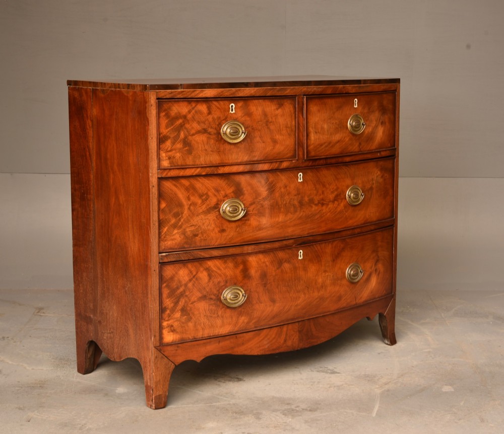 A Georgian flame mahogany bowfront chest of drawers featuring two short over two long drawers with brass ring handles and splayed bracket feet. View IV