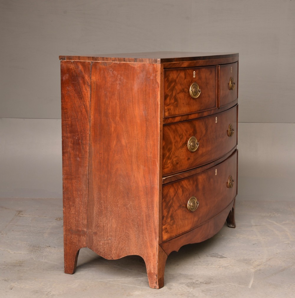 A Georgian flame mahogany bowfront chest of drawers featuring two short over two long drawers with brass ring handles and splayed bracket feet. View V