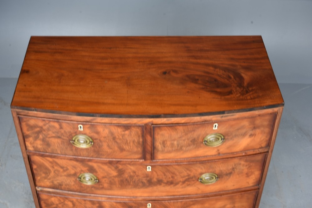 A Georgian flame mahogany bowfront chest of drawers featuring two short over two long drawers with brass ring handles and splayed bracket feet. View VI