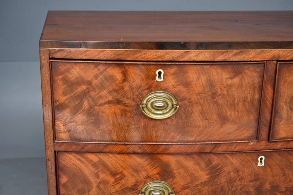 A Georgian flame mahogany bowfront chest of drawers featuring two short over two long drawers with brass ring handles and splayed bracket feet. View VII