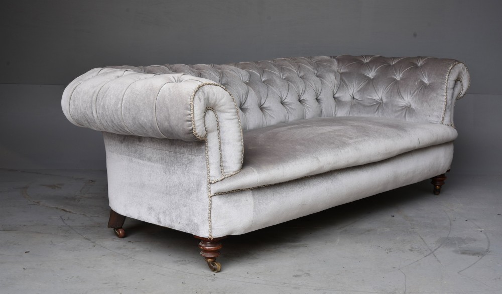 A grey velvet Victorian Chesterfield sofa featuring deep-buttoned upholstery, low rolled arms, stud trim, and turned wood legs with brass casters. View III
