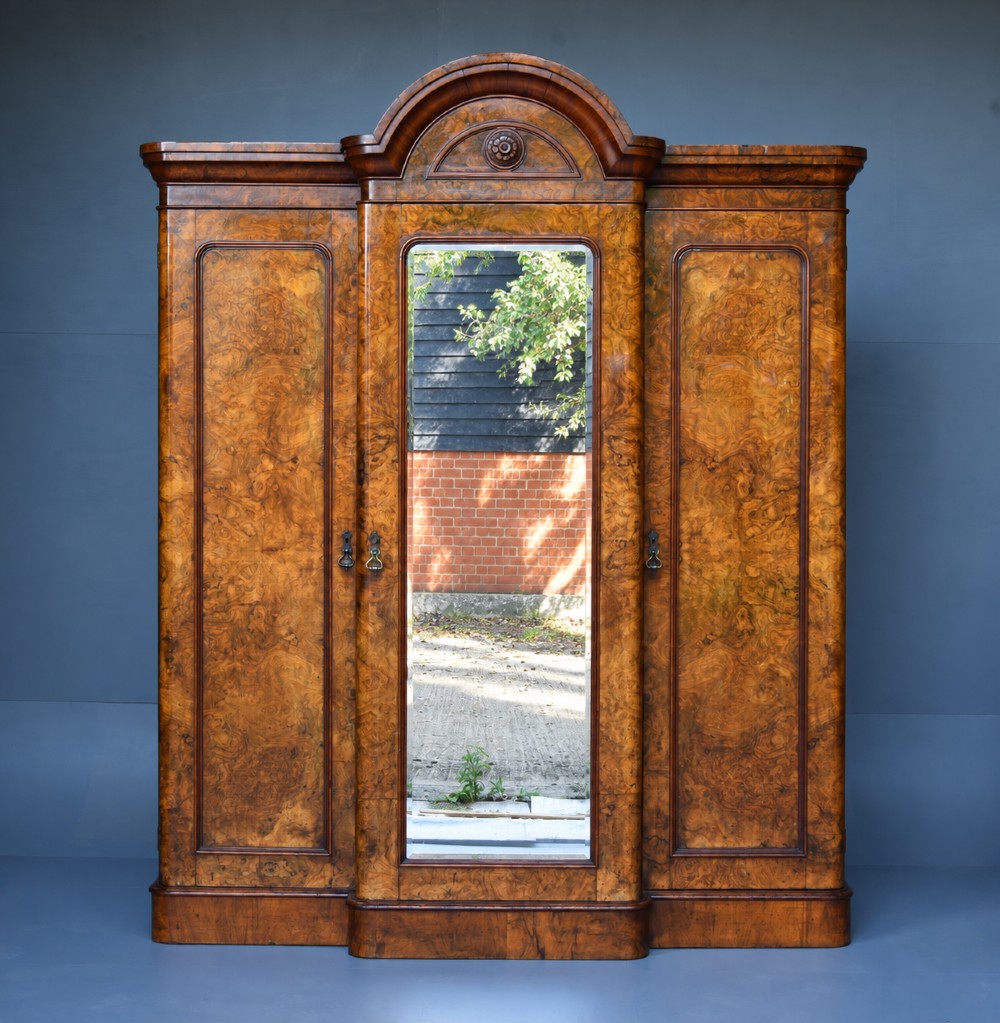 A Victorian burr walnut triple wardrobe featuring an arched central mirrored door flanked by two panelled timber doors with carved mouldings.