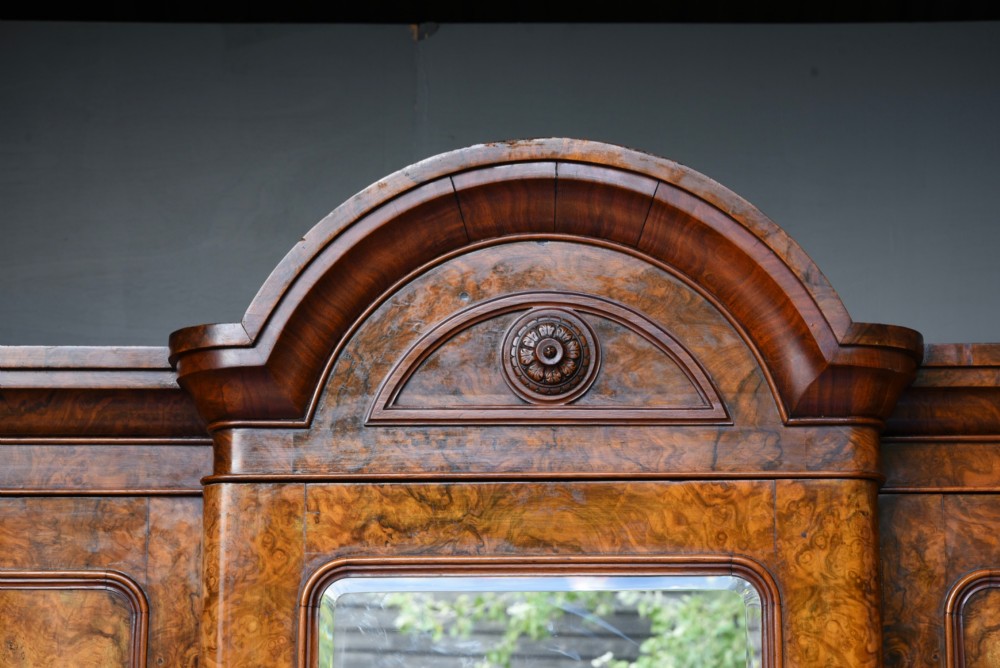 A Victorian burr walnut triple wardrobe featuring an arched central mirrored door flanked by two panelled timber doors with carved mouldings. View V