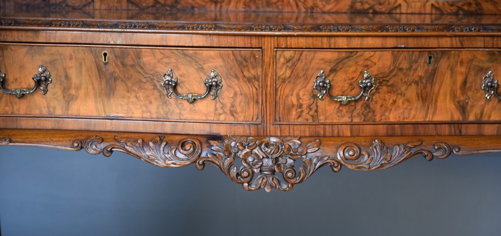 A Queen Anne style burr walnut side table featuring two drawers with brass handles, carved cabriole legs, and a raised gallery top. View IV