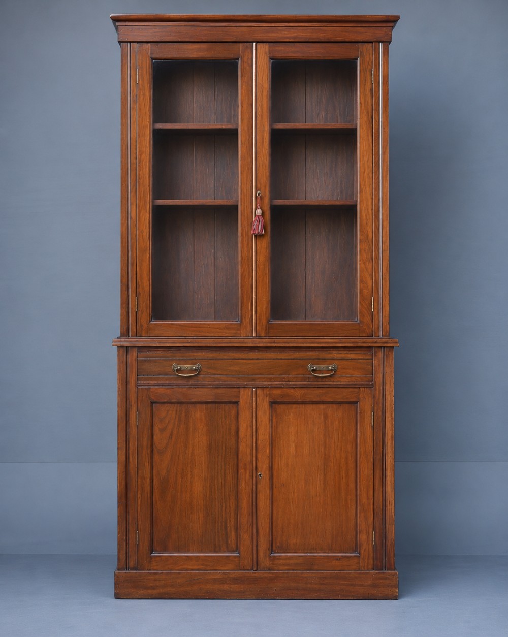 A tall Victorian walnut bookcase featuring upper glazed doors, a central drawer with brass drop handles, and lower solid panelled cupboard doors.