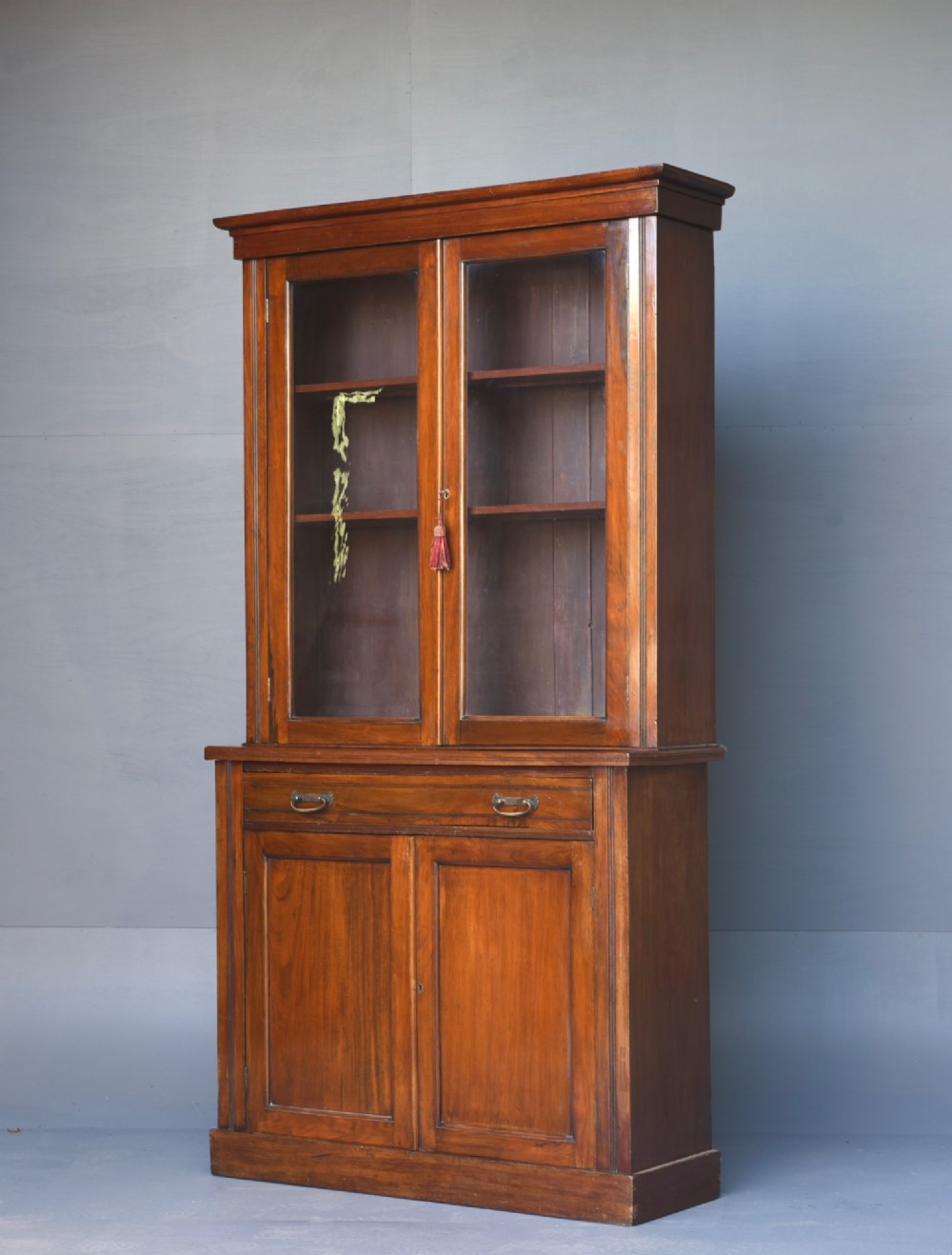 A tall Victorian walnut bookcase featuring upper glazed doors, a central drawer with brass drop handles, and lower solid panelled cupboard doors. View II