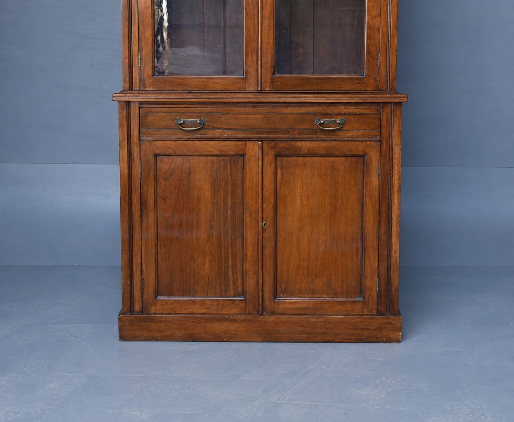 A tall Victorian walnut bookcase featuring upper glazed doors, a central drawer with brass drop handles, and lower solid panelled cupboard doors. View III