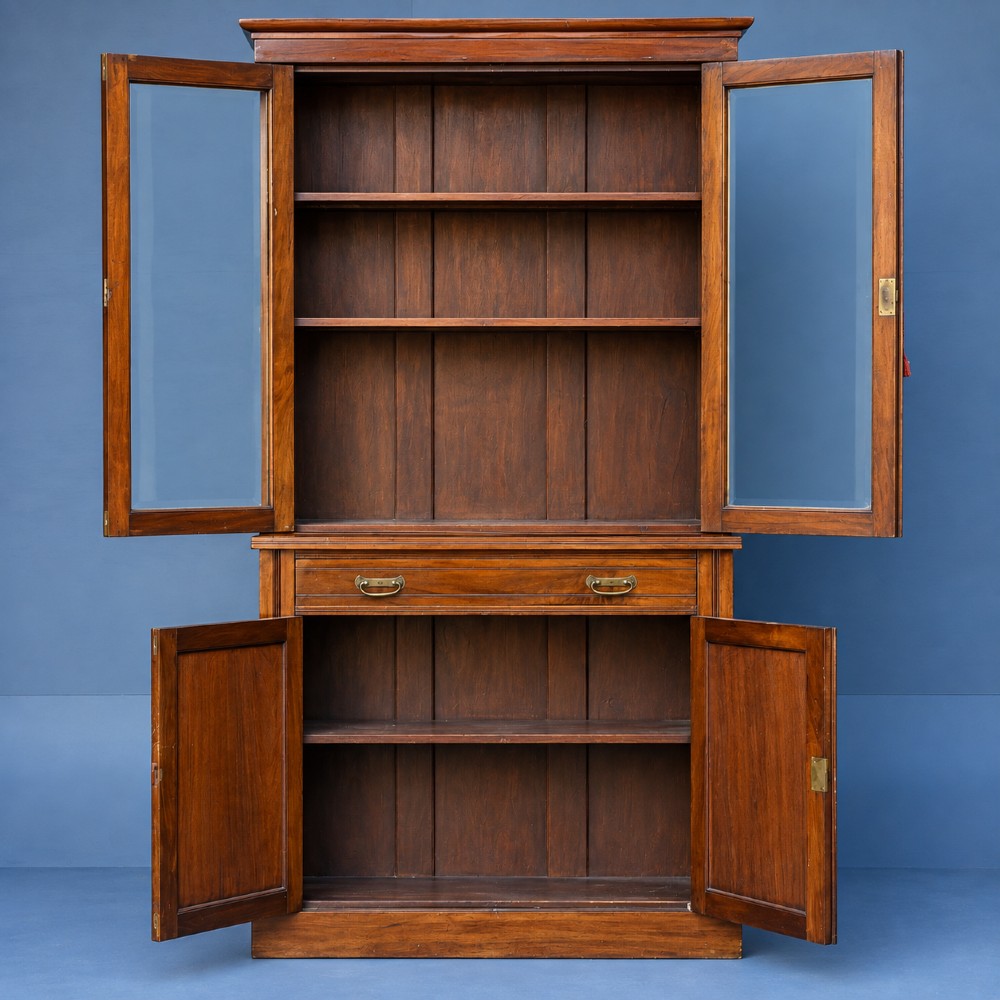 A tall Victorian walnut bookcase featuring upper glazed doors, a central drawer with brass drop handles, and lower solid panelled cupboard doors. View IV