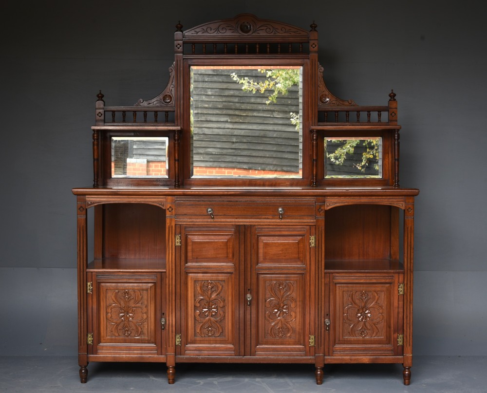 A carved Victorian walnut sideboard with a three-panel mirrored superstructure, spindle galleries, and lower cupboard doors decorated with floral carved panels.