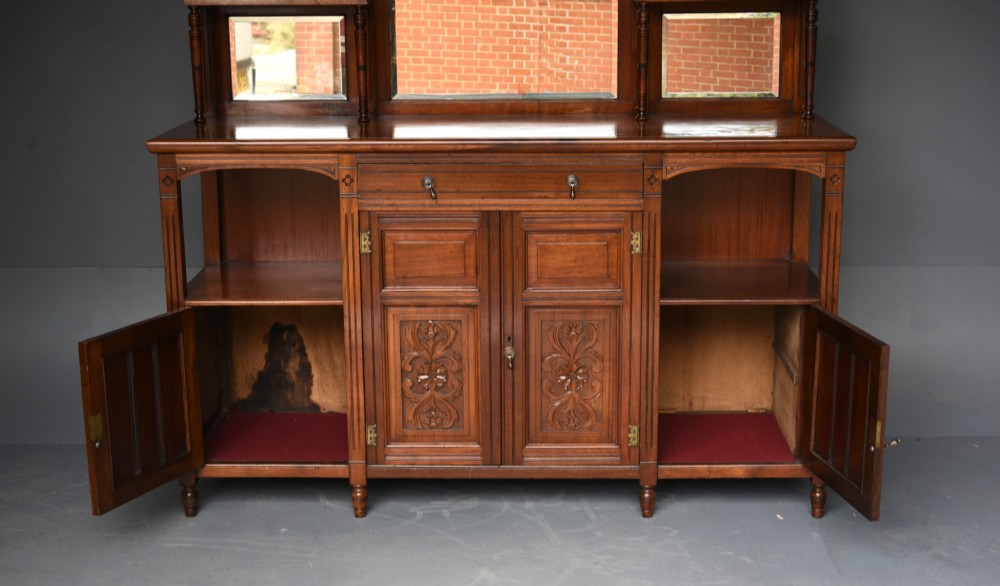 A carved Victorian walnut sideboard with a three-panel mirrored superstructure, spindle galleries, and lower cupboard doors decorated with floral carved panels. View V
