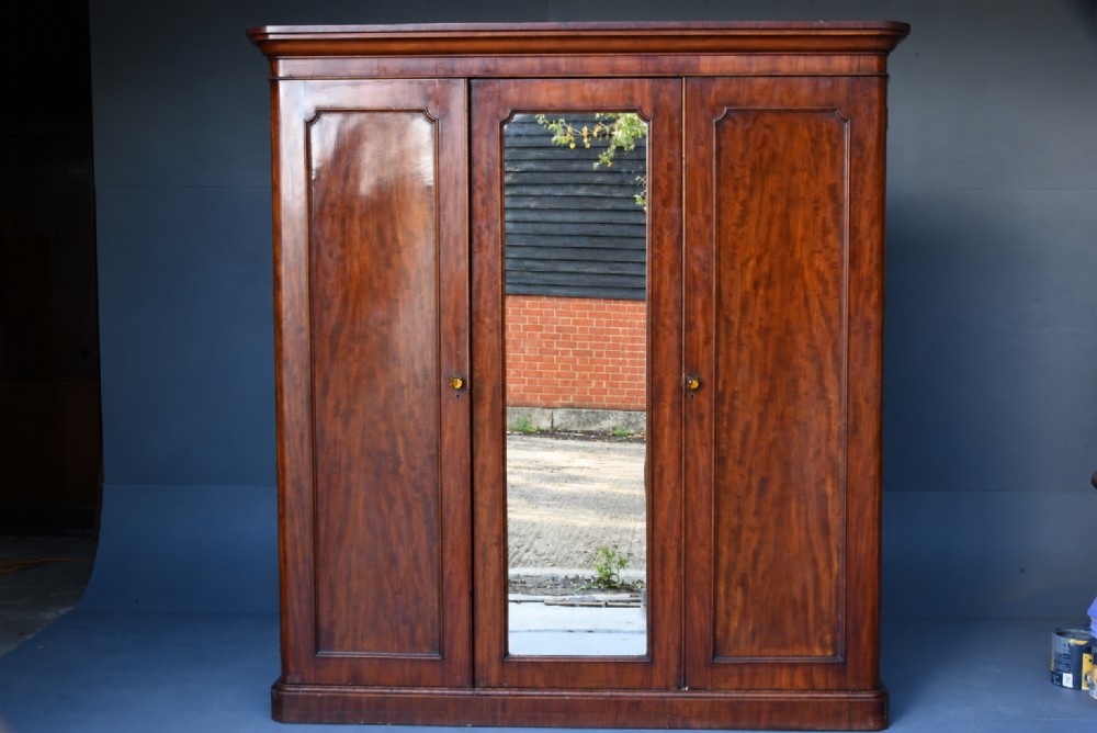 A Victorian mahogany triple wardrobe featuring two outer panelled doors, a central mirrored door, and a moulded cornice top.