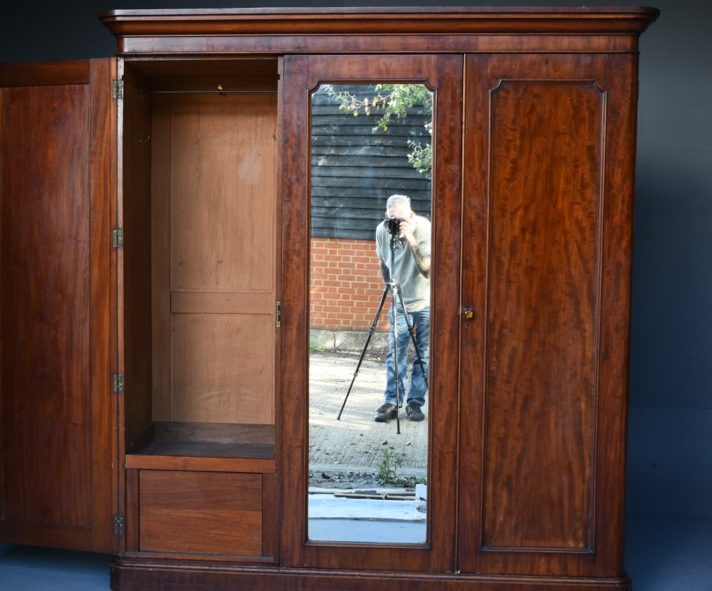 A Victorian mahogany triple wardrobe featuring two outer panelled doors, a central mirrored door, and a moulded cornice top. View II