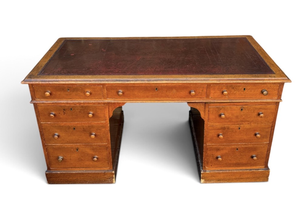 A Victorian oak pedestal desk featuring a red leather inset top, wooden knob handles, and multiple drawers on twin pedestals.