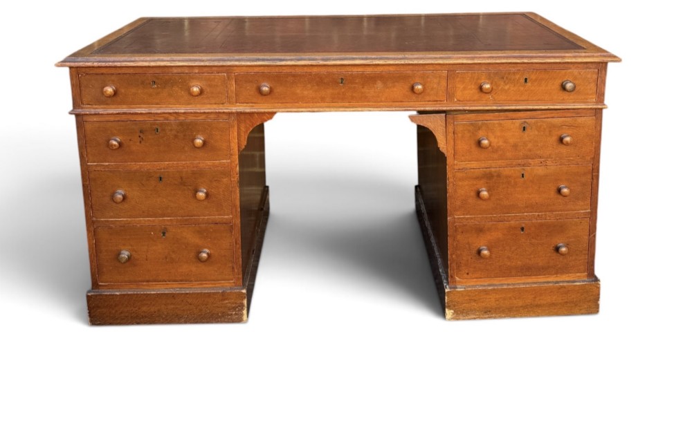 A Victorian oak pedestal desk featuring a red leather inset top, wooden knob handles, and multiple drawers on twin pedestals. View II