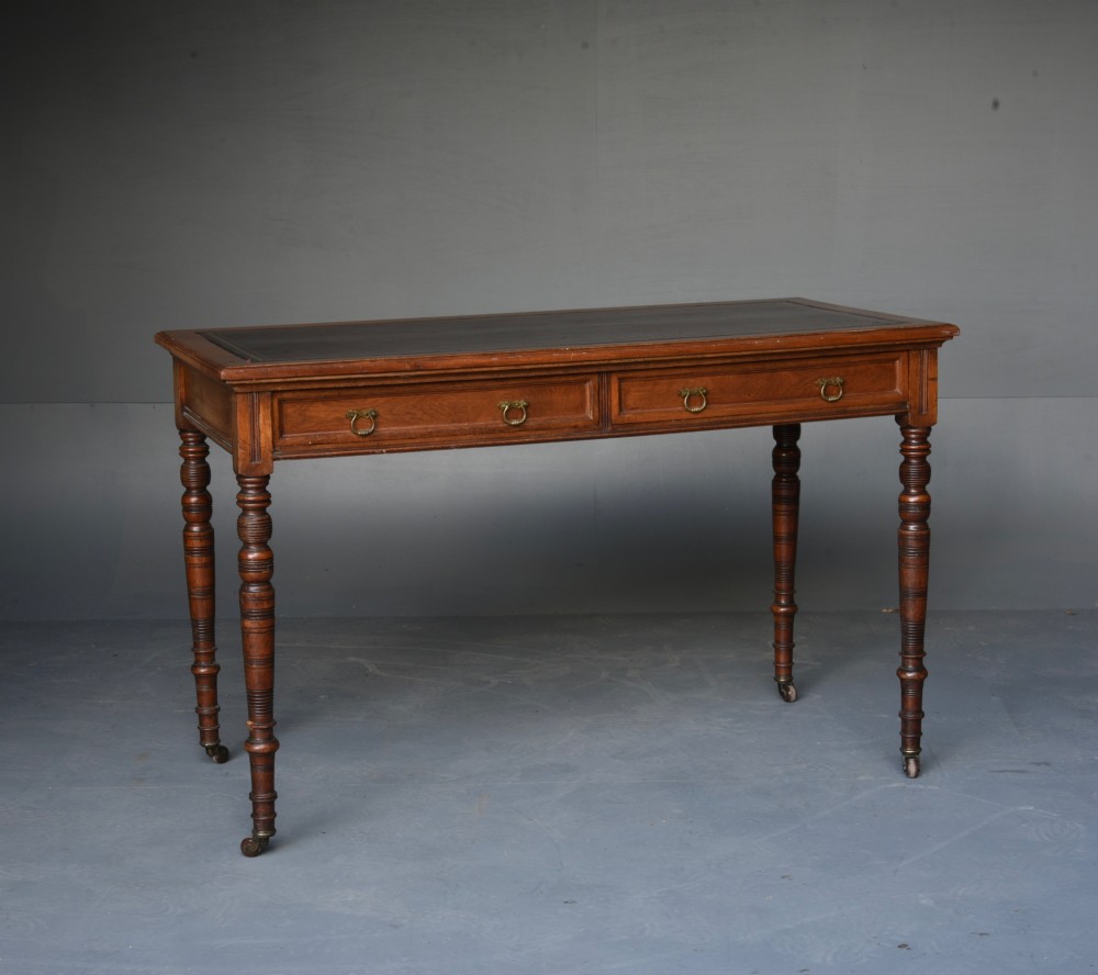 A Victorian walnut writing table featuring a dark leather top, two frieze drawers with brass handles, and slender turned legs ending in castors.