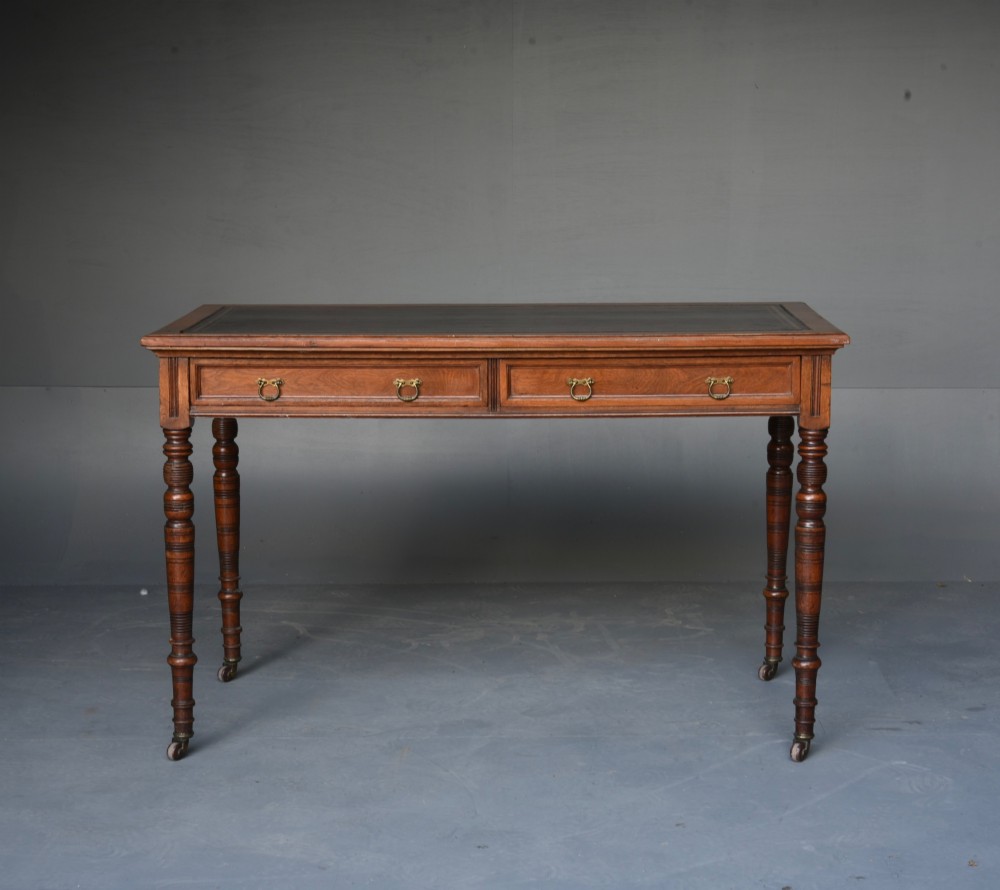 A Victorian walnut writing table featuring a dark leather top, two frieze drawers with brass handles, and slender turned legs ending in castors. View II