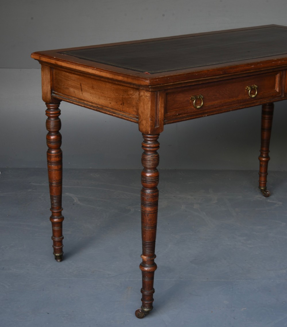 A Victorian walnut writing table featuring a dark leather top, two frieze drawers with brass handles, and slender turned legs ending in castors. View III