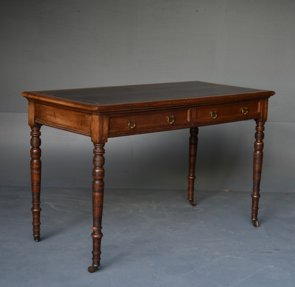 A Victorian walnut writing table featuring a dark leather top, two frieze drawers with brass handles, and slender turned legs ending in castors. View IV