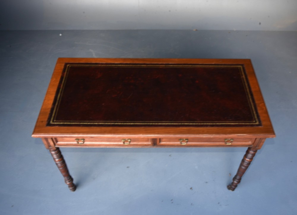 A Victorian walnut writing table featuring a dark leather top, two frieze drawers with brass handles, and slender turned legs ending in castors. View V