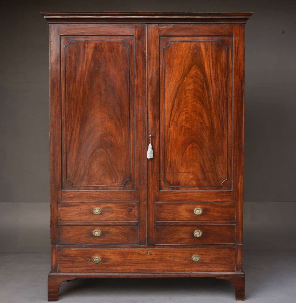 A Georgian mahogany double wardrobe featuring flame mahogany door panels, three lower drawers with brass drop handles, and bracket feet.