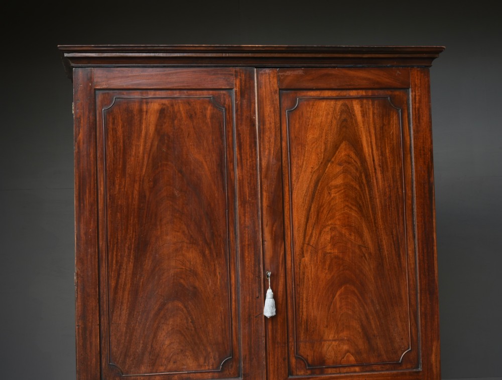 A Georgian mahogany double wardrobe featuring flame mahogany door panels, three lower drawers with brass drop handles, and bracket feet. View II