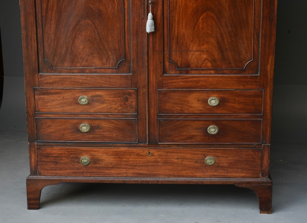 A Georgian mahogany double wardrobe featuring flame mahogany door panels, three lower drawers with brass drop handles, and bracket feet. View III
