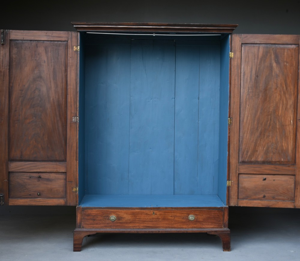 A Georgian mahogany double wardrobe featuring flame mahogany door panels, three lower drawers with brass drop handles, and bracket feet. View IV