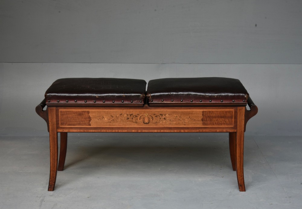A 19th-century inlaid mahogany duet piano stool featuring two dark brown leather padded seats trimmed with brass studs and central foliate marquetry along the front frame.