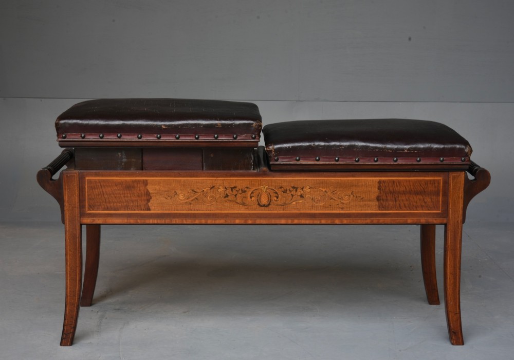 A 19th-century inlaid mahogany duet piano stool featuring two dark brown leather padded seats trimmed with brass studs and central foliate marquetry along the front frame. View II