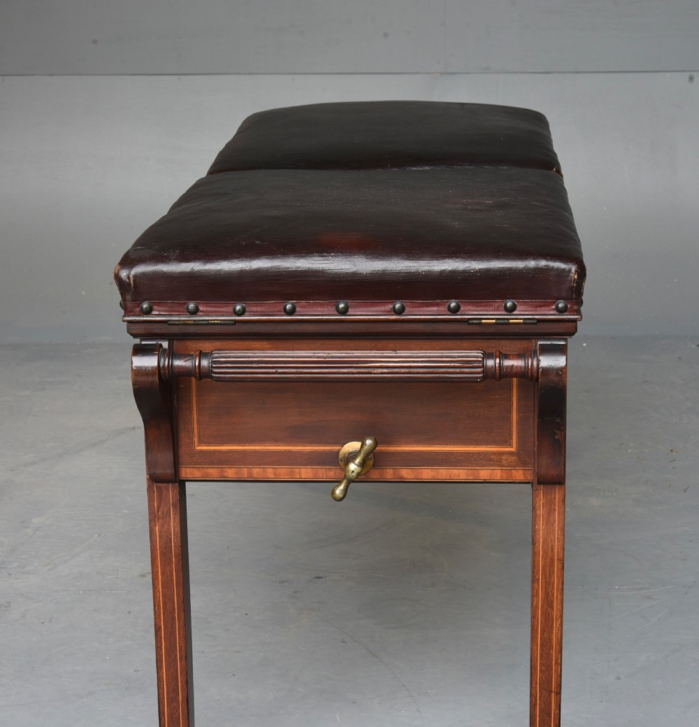 A 19th-century inlaid mahogany duet piano stool featuring two dark brown leather padded seats trimmed with brass studs and central foliate marquetry along the front frame. View III