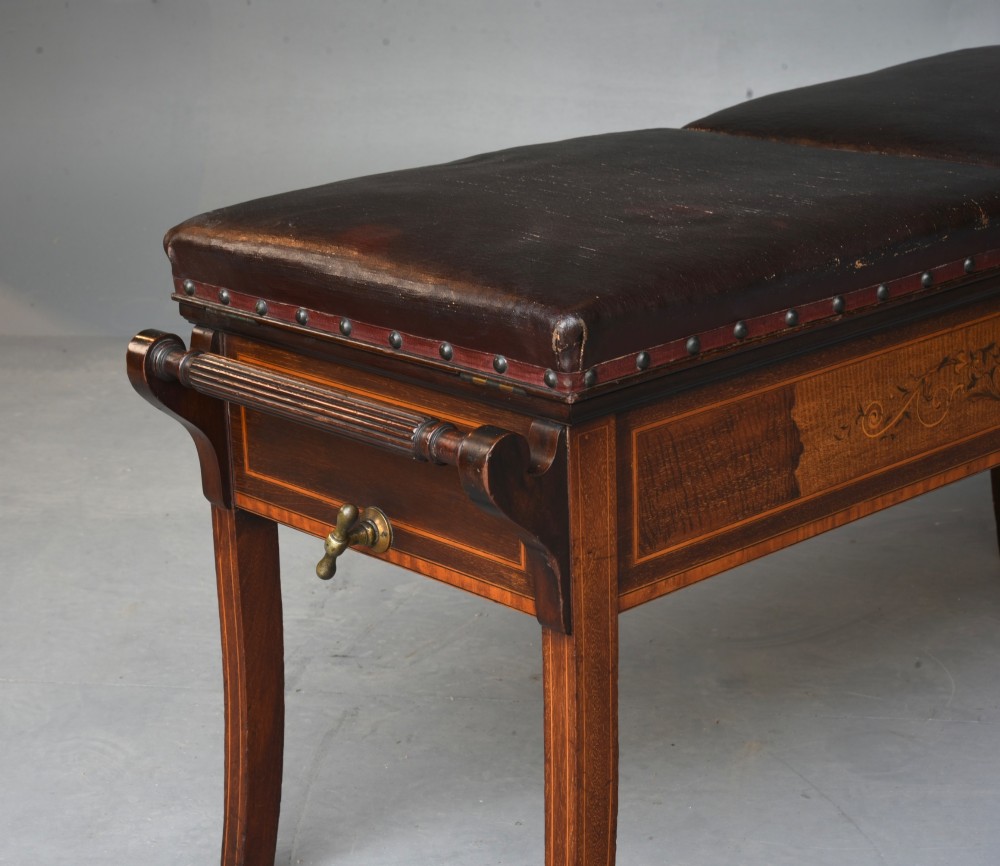 A 19th-century inlaid mahogany duet piano stool featuring two dark brown leather padded seats trimmed with brass studs and central foliate marquetry along the front frame. View IV