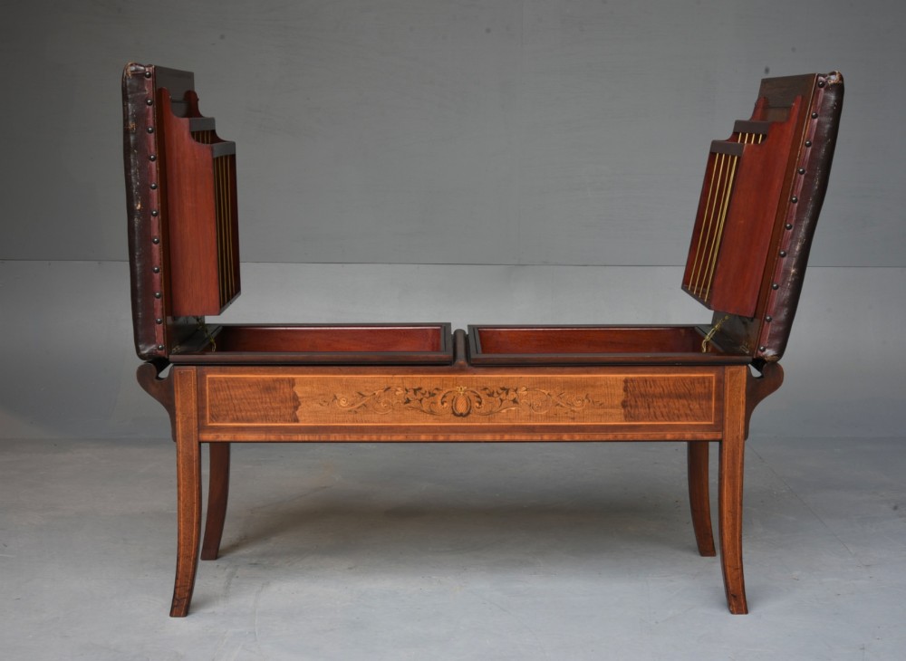 A 19th-century inlaid mahogany duet piano stool featuring two dark brown leather padded seats trimmed with brass studs and central foliate marquetry along the front frame. View V