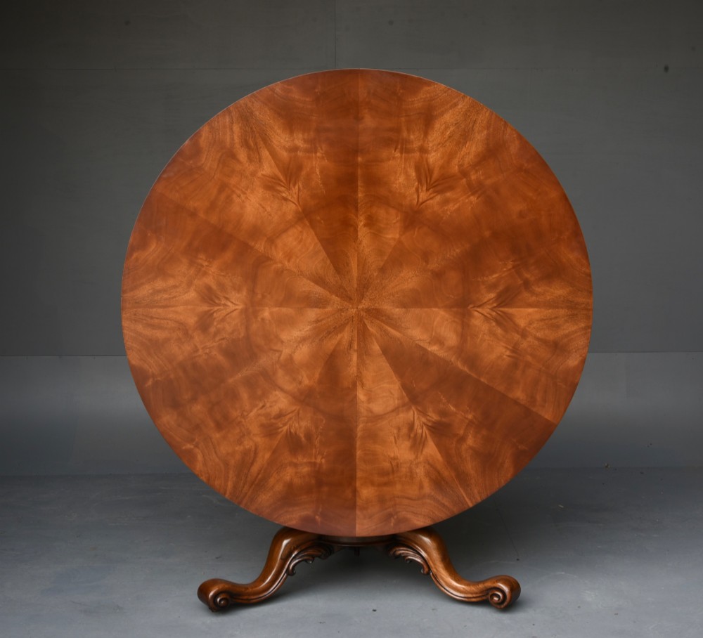 A nineteenth-century circular mahogany tilt-top table with radial flame mahogany veneering set on a carved tripod base with scroll feet.