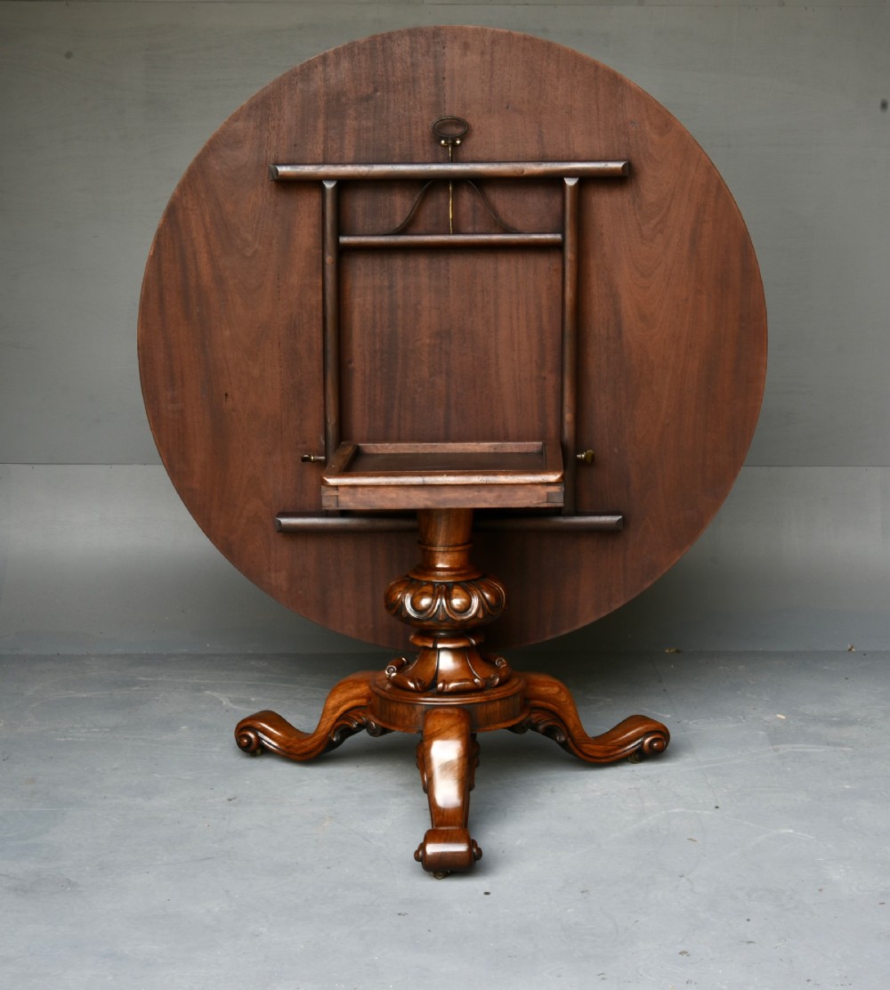 A nineteenth-century circular mahogany tilt-top table with radial flame mahogany veneering set on a carved tripod base with scroll feet. View IV